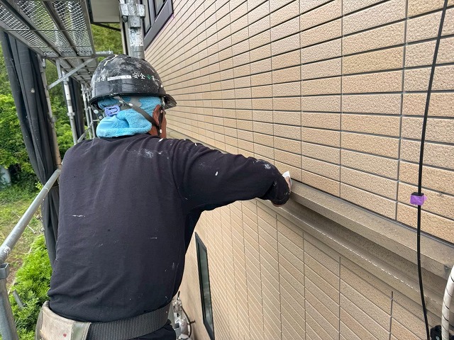 足場上で幕板の表面をサンドペーパーでケレン処理を行う職人の様子