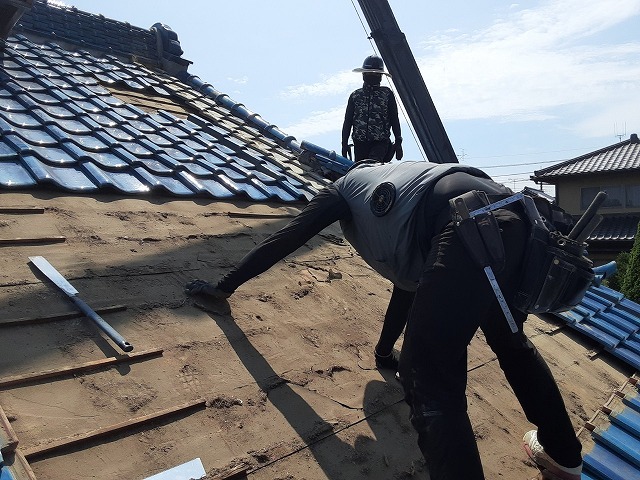 雨漏り修理のための屋根葺き直し工事で青緑瓦の取り外しを行う屋根職人