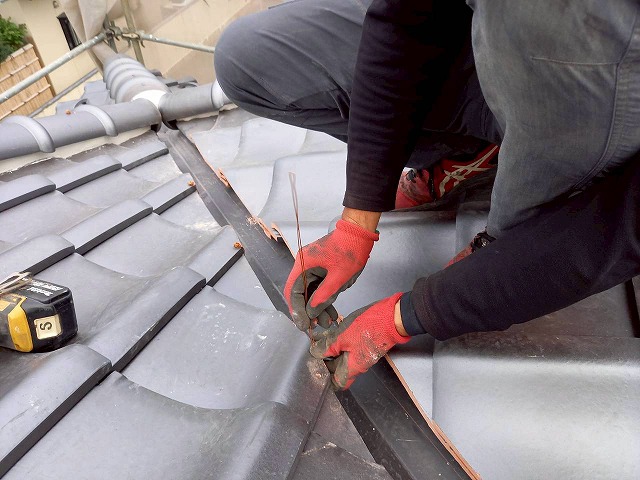 屋根葺き替え工事で勝手瓦に穴をあけて銅線で固定している状況