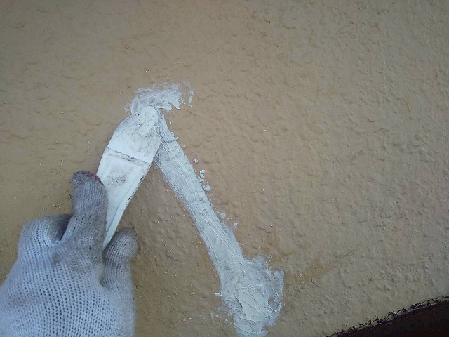 モルタル外壁塗装工事のひび割れ部分へのコーキング充填後ヘラ押さえ