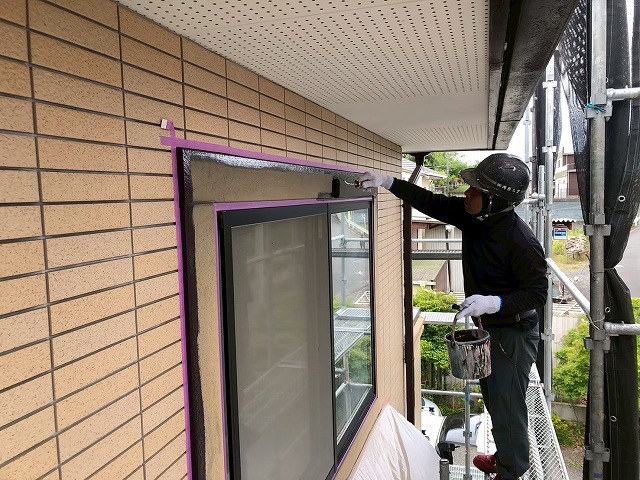 足場上で窓まわりモールにローラー塗りを行う作業員の様子
