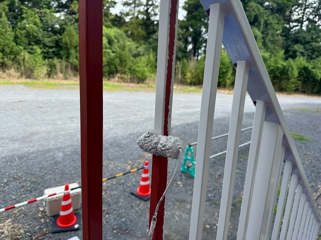 小型ローラーで鉄骨階段の手すり部分に中塗り塗料を塗布している様子