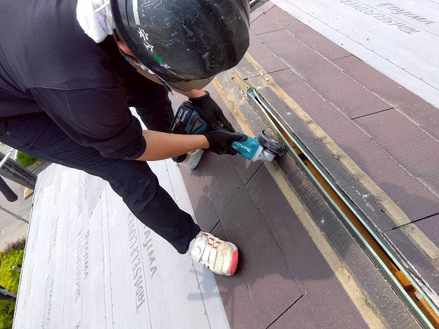 防水シート敷設の妨げとなる換気棟受け金具の出っ張りをグラインダーでカットしている状況