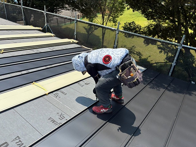 防水シート上で金属屋根材を留め付けながら葺き進める作業員の様子