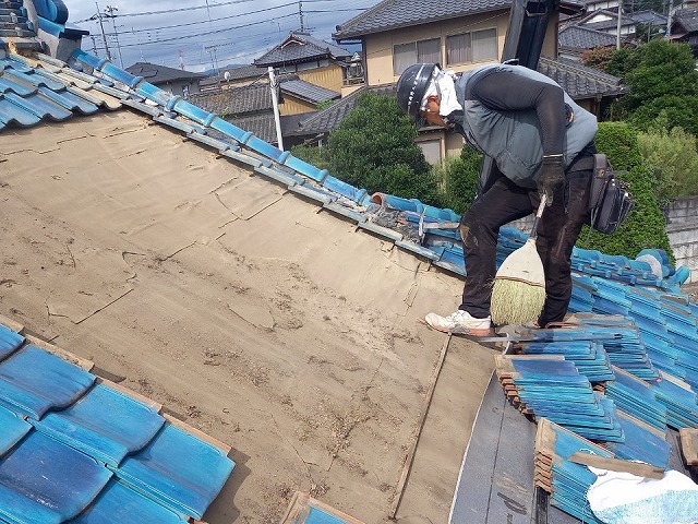 雨漏り修理のための屋根葺き直し工事で青緑瓦の取り外し後に清掃を行う屋根職人