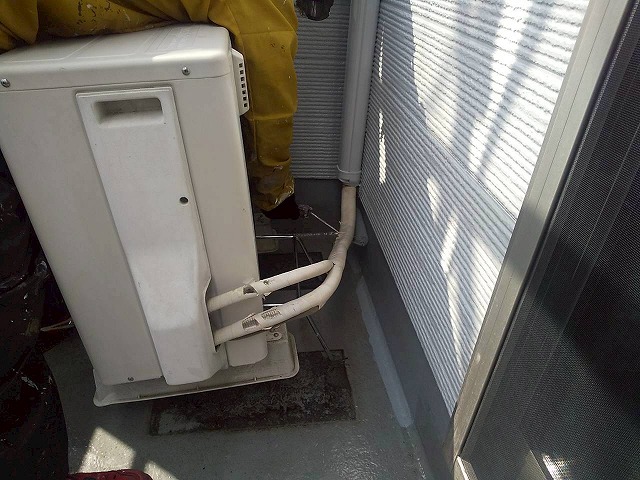 エアコン室外機を架台に載せて浮かせ、裏側や下側までAUコートを塗装している様子