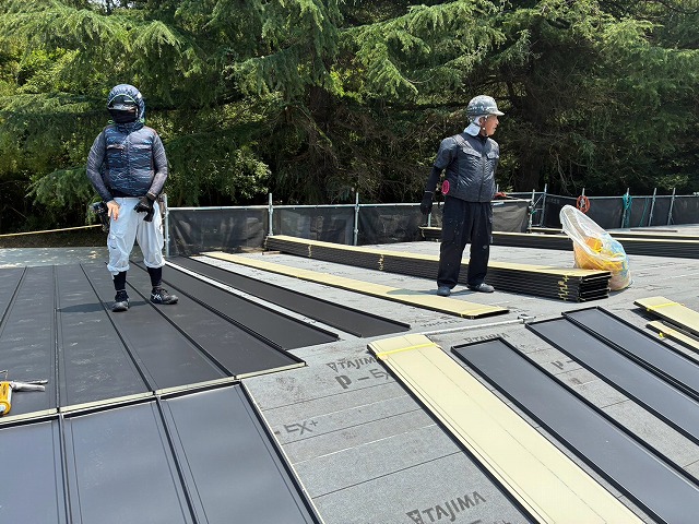屋根材を並べて施工を進める作業員と屋根上に置かれた屋根材の様子