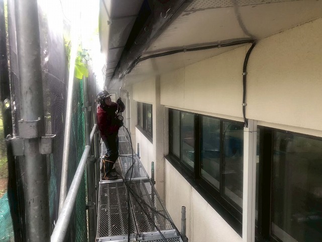 足場上から軒天や鼻隠しなどを高圧洗浄している様子