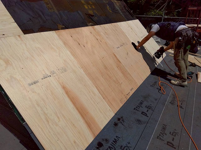 三角屋根の斜面に新しい構造用合板を釘打ちで張り付ける職人