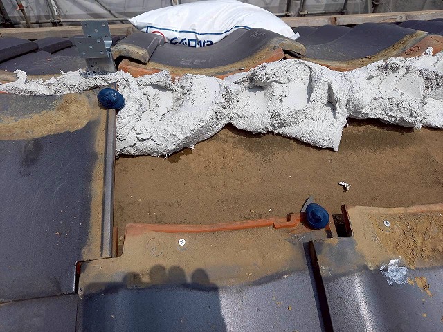 下屋根の棟取り直し工事で瓦材にズレ防止のコーキングを打設している状況