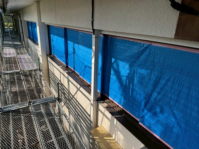 ブルーシートで養生された窓と足場が架けられたSRC造建物の外壁